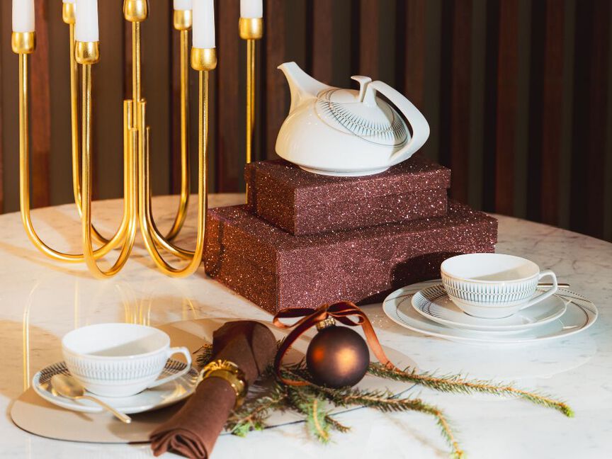 Weihnachtlich dekorierter Tisch mit modernem weißem Porzellanset von Rosenthal, glitzernden Geschenkboxen und Christbaumkugel.