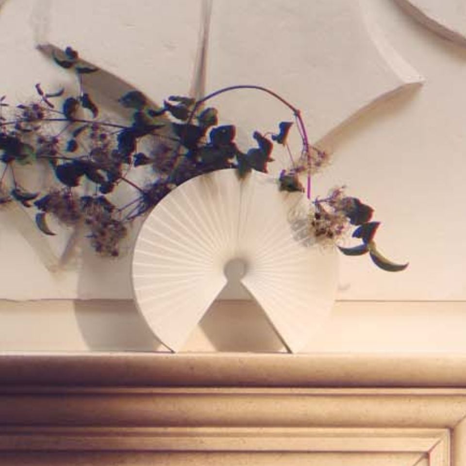 A sculptural white porcelain vase with flowing, ruffled edges on a dark wood shelf.