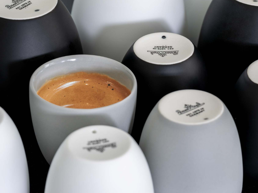 Tasses &agrave; caf&eacute; Rosenthal aux formes &eacute;pur&eacute;es et modernes, sans anse, silhouette cylindrique avec bord l&eacute;g&egrave;rement arrondi, partiellement empil&eacute;es et remplies d'expresso, mises en sc&egrave;ne dans un contraste noir et blanc.
