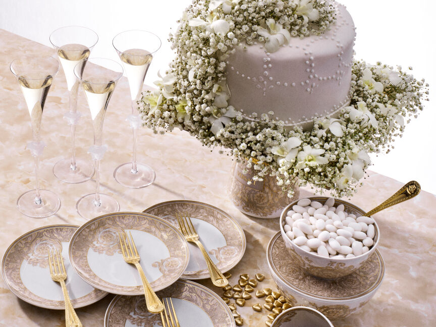 Festive table setting with Rosenthal Versace tableware with gold decoration, wedding cake with flowers, champagne glasses and bowls with almonds