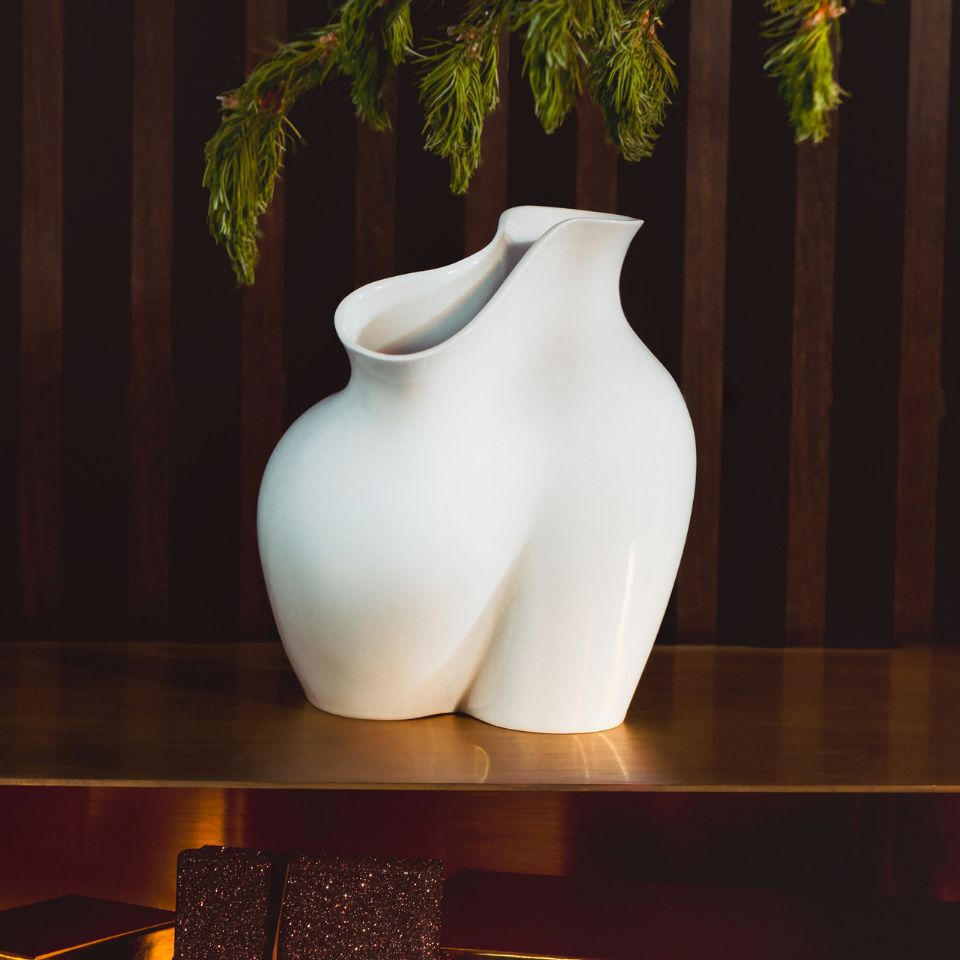 A matte white sculptural vase with organic curves, glowing under soft light.