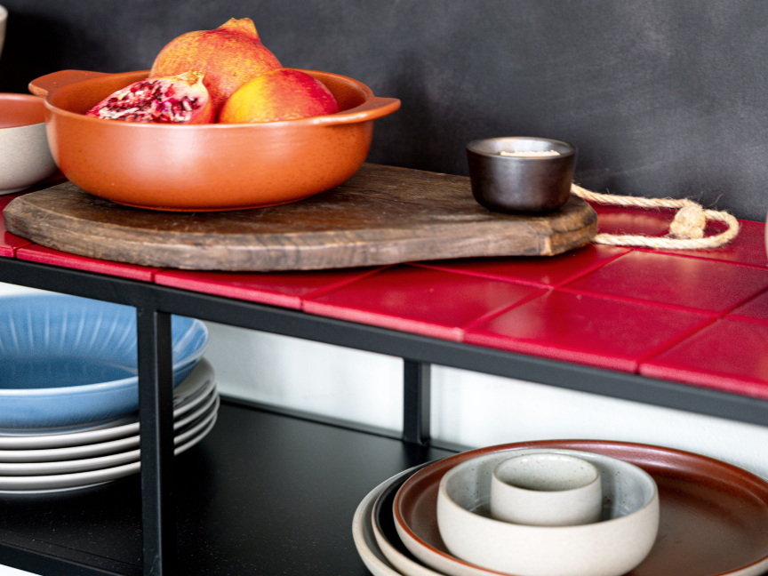 Rosenthal bowls on a wooden board set on a red tiled surface, with plates and bowls in shades of blue, beige and brown stacked underneath.
