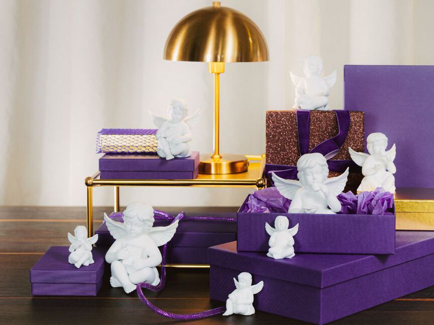 Weihnachtliche Geschenkarrangement mit lila Geschenkboxen und weißen Engel-Figuren vor goldener Tischlampe.