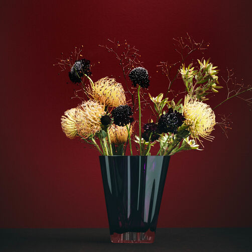 Flux Glasvase in Berry mit unterschiedlichen Blumen gef&uuml;llt steht vor einem dunkelrotem Hintergrund