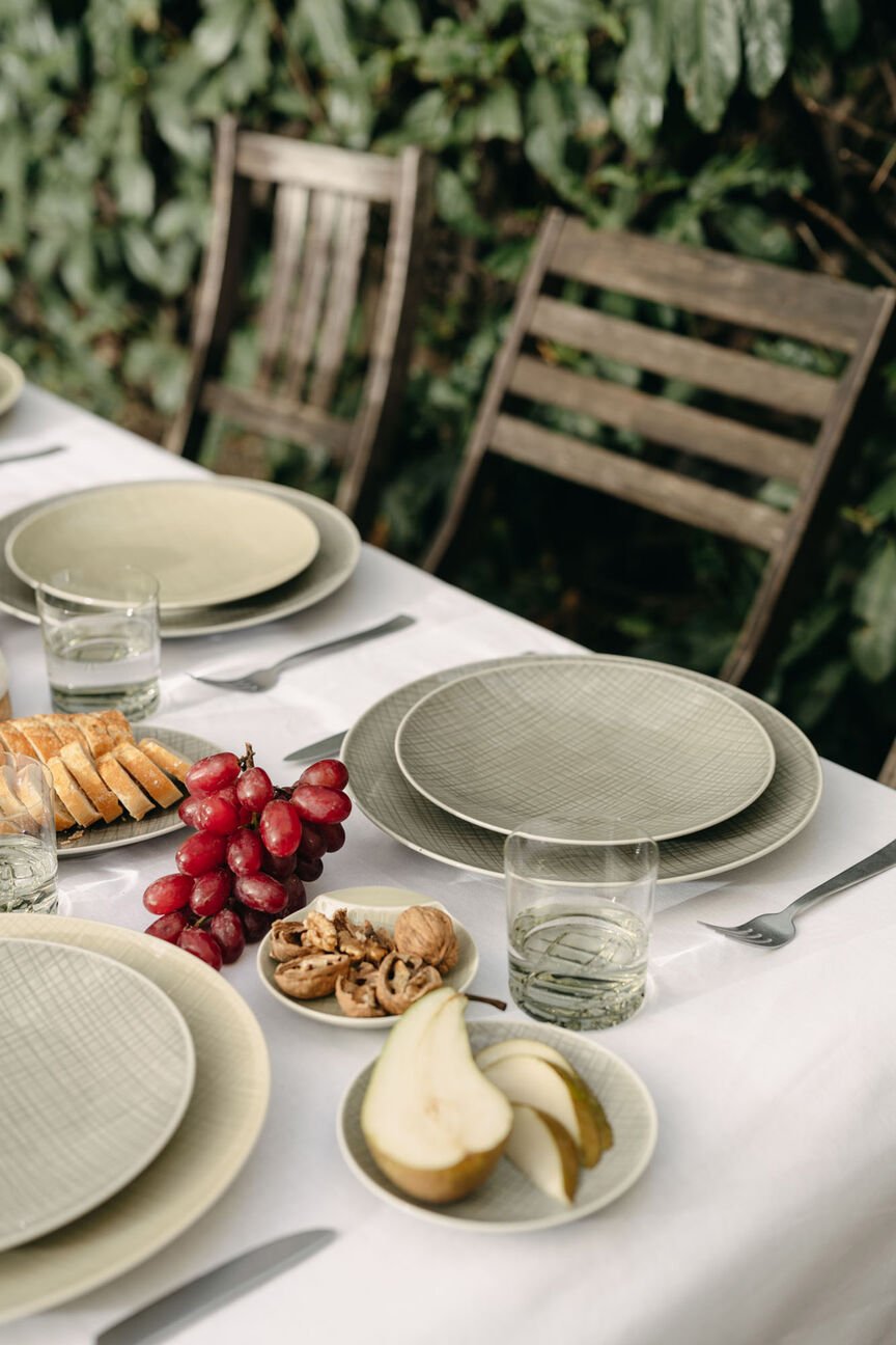 Rosenthal Mesh Dining Collection Gedeckter Tisch im Garten mit unterschiedlichen Mesh Mountain und Cream Tellern, Mesh Gläsern und Obst, Nüssen und Baguette.