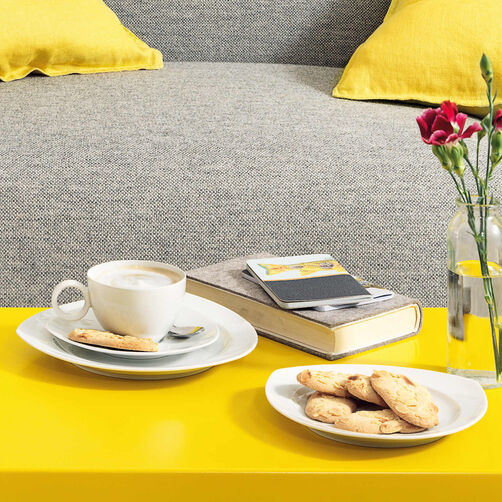 Thomas Vario Thomas Vario cup filled with capuccino, plates with cookies on yellow couch table in front of a grey couch