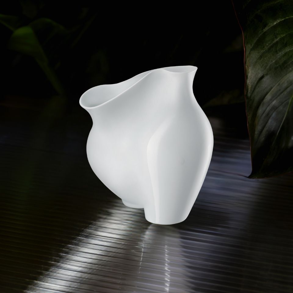 A matte white sculptural vase with organic curves, glowing under soft light.