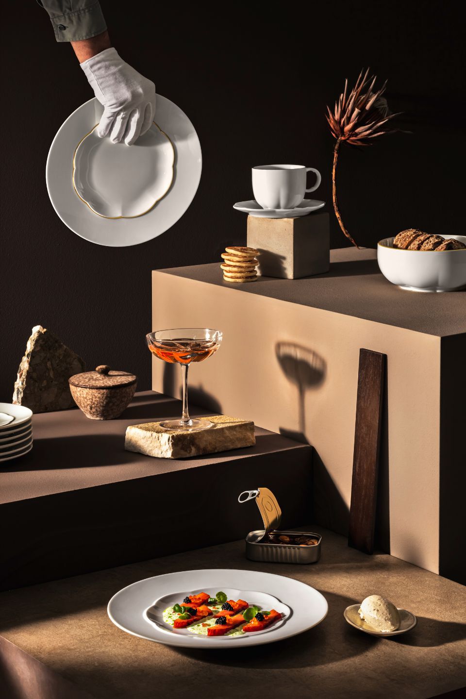 Sonetto Collection Elegant Sonetto porcelain tableware in a modern still life arrangement, featuring white plates with gold-edged contours, a teacup, dessert bowls, and a cocktail glass, styled with gourmet food and artistic props on tiered neutral-toned surfaces.