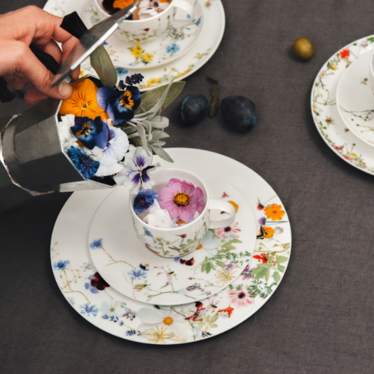 Rosenthal-Geschirr mit filigranem Blumenmuster, befüllt mit bunten Blüten und stilvoll arrangiert auf dunkler Tischdecke.