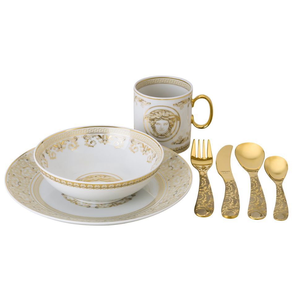 Versace porcelain dining set including a dinner plate, soup bowl, and Medusa-embossed mug, paired with five gold-toned cutlery pieces featuring intricate baroque engravings, all arranged on a white background.