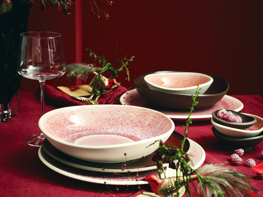 Verschiedene Junto Rose Quartz und Bronze Teller aufeinander gestapelt auf festlich gedecktem Weihnachtstisch mit S&uuml;&szlig;igkeiten und Dekozweigen