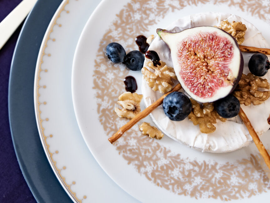 Nahaufnahme eines dekorativ angerichteten Tellergerichts mit Feige, Blaubeeren, Walnüssen und Ziegenkäse auf elegantem Porzellan.