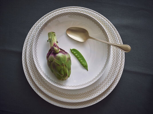 Elegante Platzteller, Speiseteller und Suppenteller aufeinander gestellt mit einer Artischoke von oben fotografiert