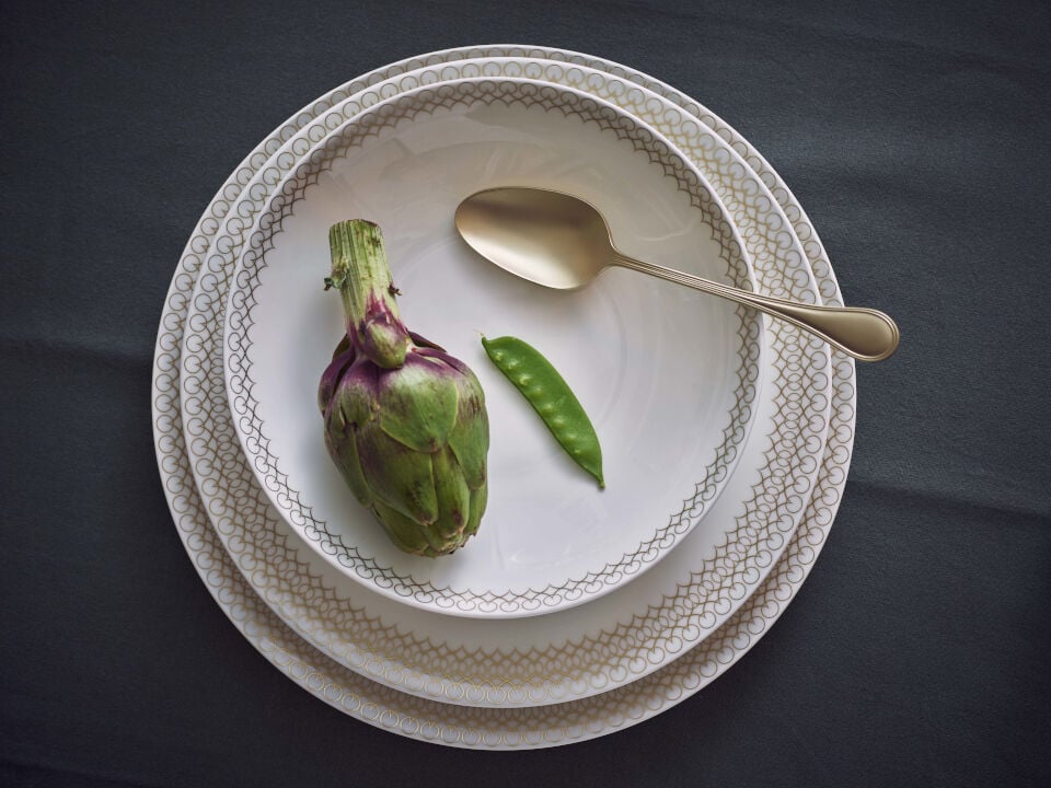 Drei Teller von Jade Glam mit goldenem L&ouml;ffel und Artischoke auf dunkler Tischdecke von oben fotogratiert