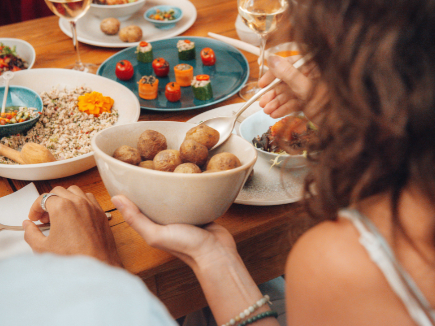 A shared meal at a wooden table, served on Rosenthal antipasti tableware. Small starters, potatoes and dips are served on colourful ceramic plates and bowls in shades of blue and natural tones.