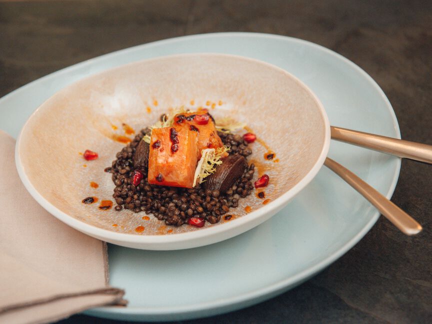 Piatto in gres di Rosenthal con portata: salmone su lenticchie, servito su un piatto color pastello con posate dorate.