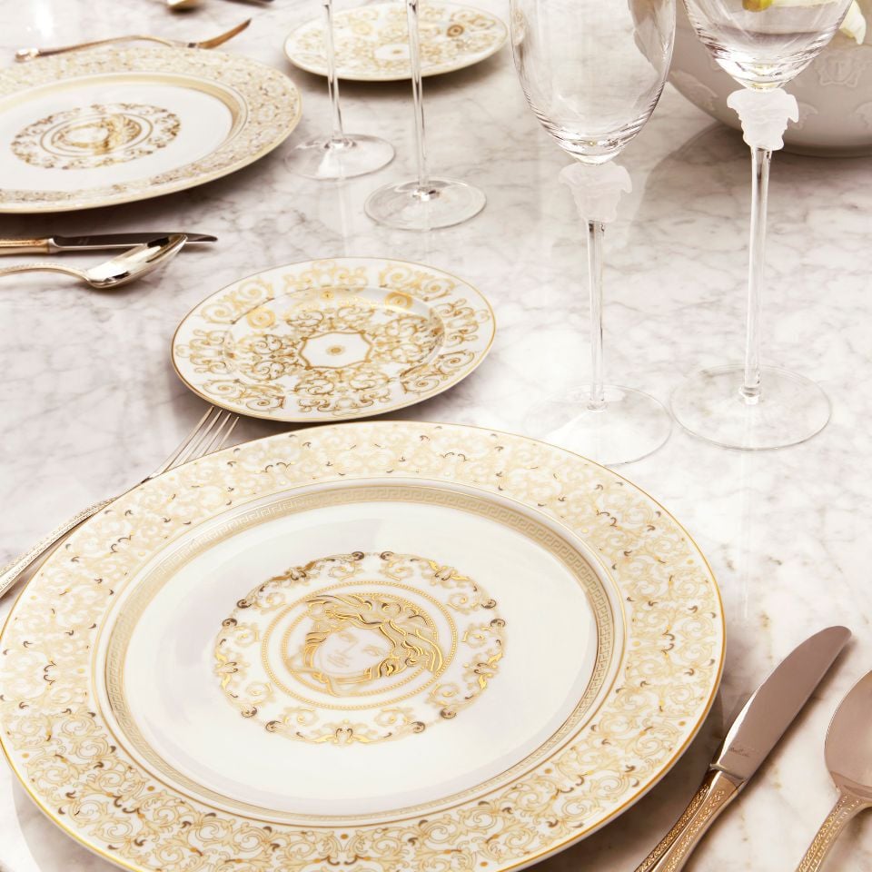 Sophisticated Versace Medusa Gala Gold table setting with ivory and gold porcelain plates, ornate scroll patterns, and the signature Medusa emblem, styled on a white marble surface.