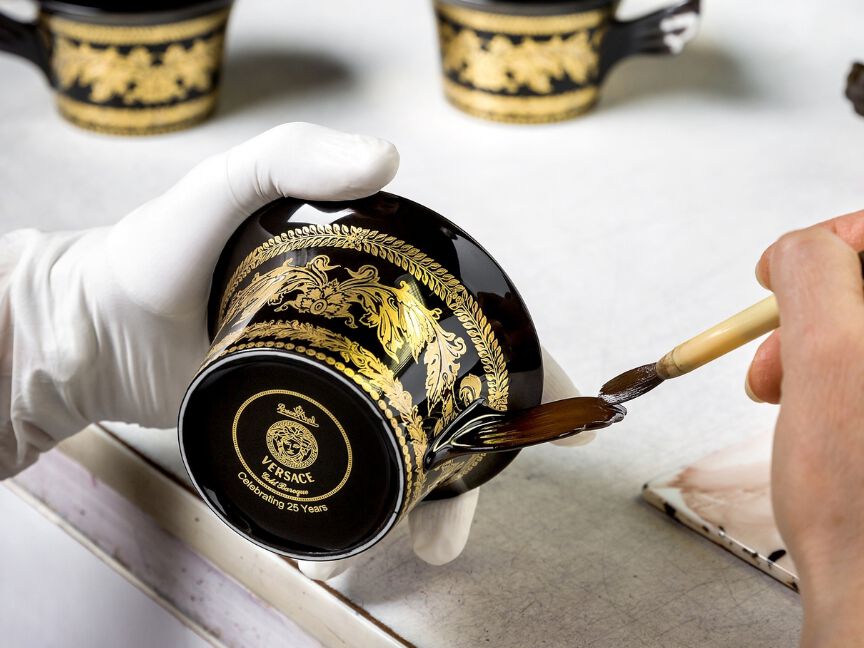 Eine schwarze Tasse mit goldenen Verzierungen wird glasiert und von Hand mit einem Pinsel vollendet.