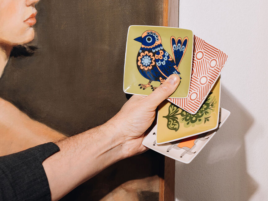 A hand holds artistically designed Rosenthal plates featuring colourful, graphic motifs &ndash; a creative and modern wedding gift idea for design enthusiasts.
