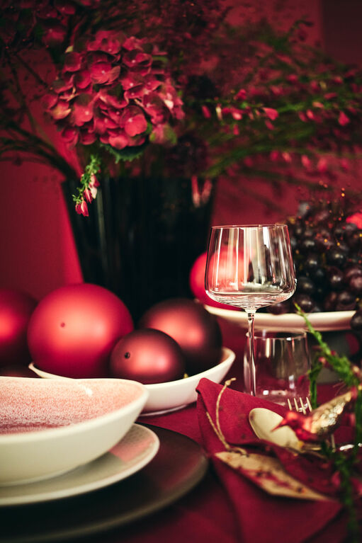 Dunkelrote Blumenarrangements und rote Weihnachtskugeln als Dekoelemente neben Junto Schalen und Turandot Weinglas