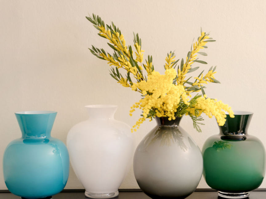 Gelbe Mimosen in farbiger Rosenthal Glasvase, umgeben von weiteren Glasvasen