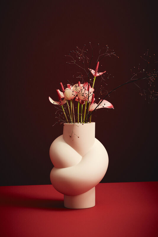 Knotenvase Node in Cameo mit rosa Blumenarrangement vor dunkelrotem Hintergrund