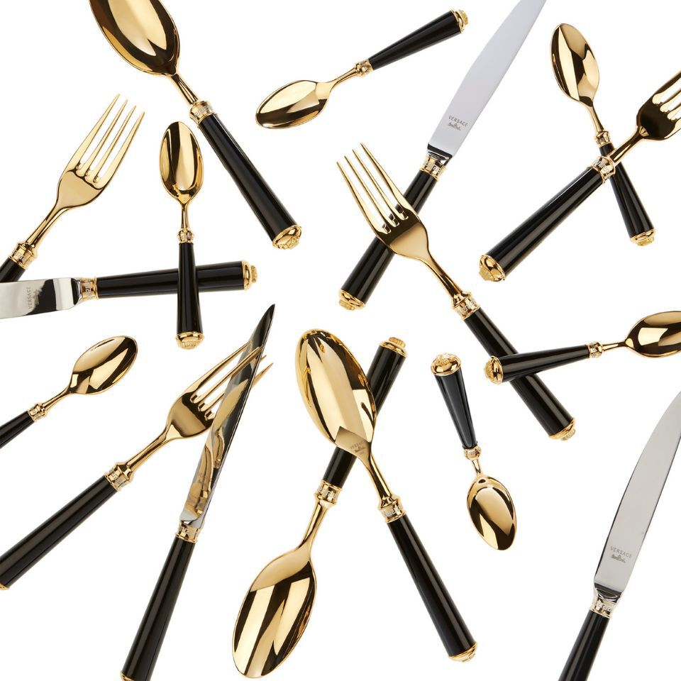 Assortment of luxurious Versace cutlery with gold-toned heads and glossy black handles, arranged in an overlapping artistic layout.