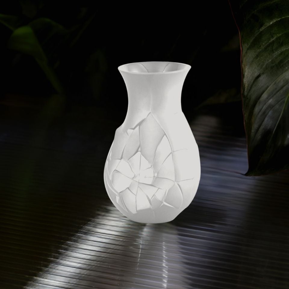 A white porcelain vase with mosaic-like shard pattern, illuminated on a dark, ribbed surface.