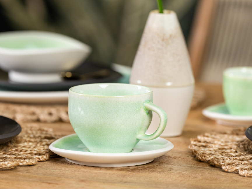 Grüne Kaffeetasse mit passender Untertasse auf gedecktem Holztisch