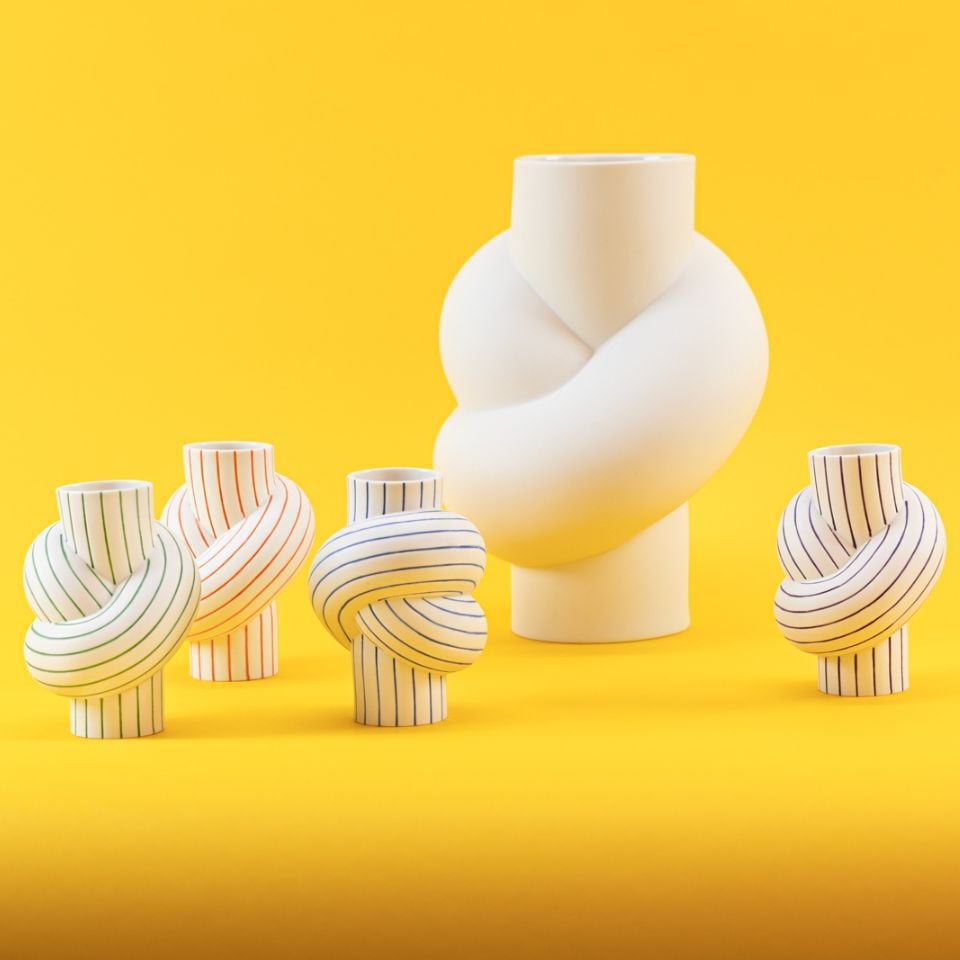 A group of vases shaped like knots in white and striped designs, set against a bright yellow backdrop.