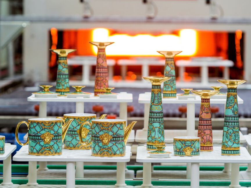 Vollst&auml;ndig dekorierte und vergoldete Porzellanst&uuml;cke werden w&auml;hrend des Endbrandes auf Gestellen vor dem Brennofen platziert.