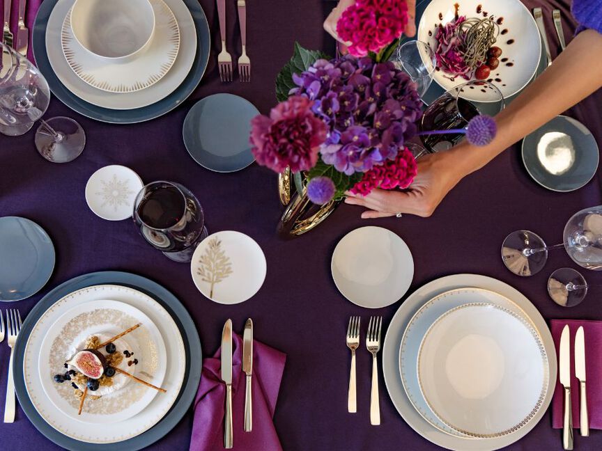 Festlich gedeckter Tisch mit lila Tischdecke, Blumen, Weingläsern und weiß-goldenen Tellern