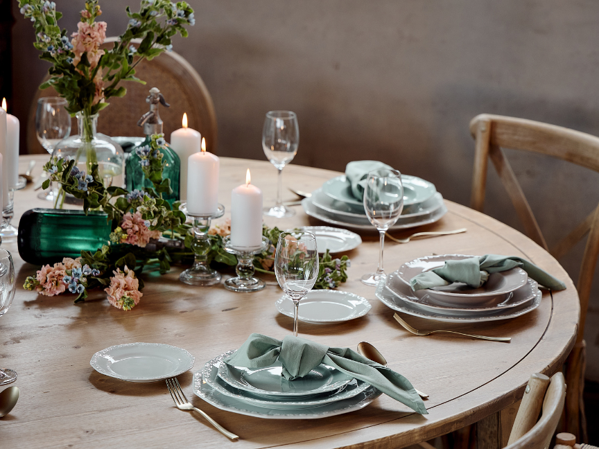 A festively laid table featuring elegant Rosenthal tableware in soft shades of green, combined with candles, glass vases and floral arrangements.