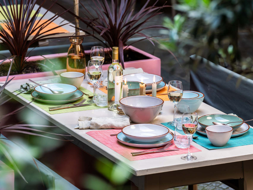 Extravagantes Rosenthal-Geschirr in sanften Pastellfarben auf stilvoll gedecktem Outdoor-Tisch mit Tellern, Schalen, Gl&auml;sern und sommerlicher Atmosph&auml;re.