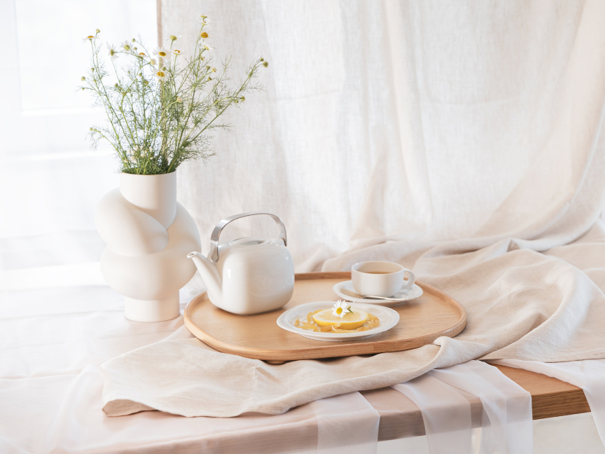 Helles Fr&uuml;hst&uuml;cksarrangement mit wei&szlig;er Teekanne, Tasse und Teller von Rosenthal mit Geb&auml;ck auf einem Holztablett.
