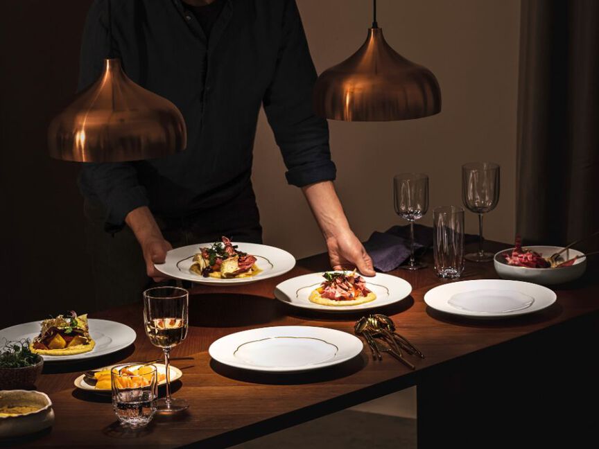 Stimmungsvoll gedeckter Dinner-Tisch mit warmem Licht, elegantem Porzellan und servierten Gerichten.