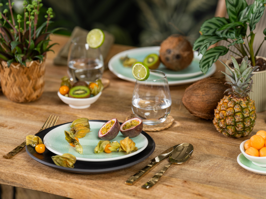 A rustic table setting featuring Rosenthal&rsquo;s antipasti tableware. Figs, citrus fruits and small starters are served on colourful ceramic plates, surrounded by tropical fruits and decorative plants.