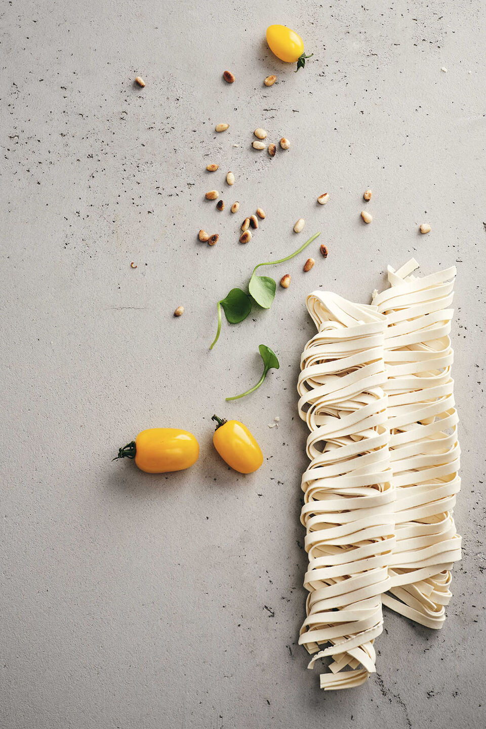 Ungekochte Tagliatelle mit Pinienkernen und gelber Beete liegen auf einem Betonuntergrund.