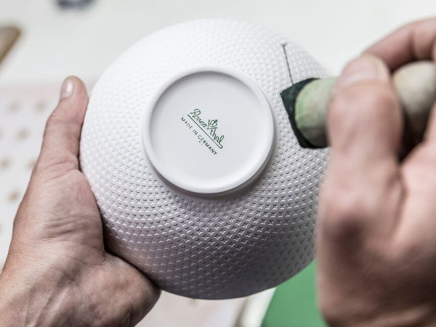 Detailaufnahme einer Rosenthal-Schale mit geprägter Oberfläche und Bodenmarke „Rosenthal – Made in Germany“, die von Hand bearbeitet wird.