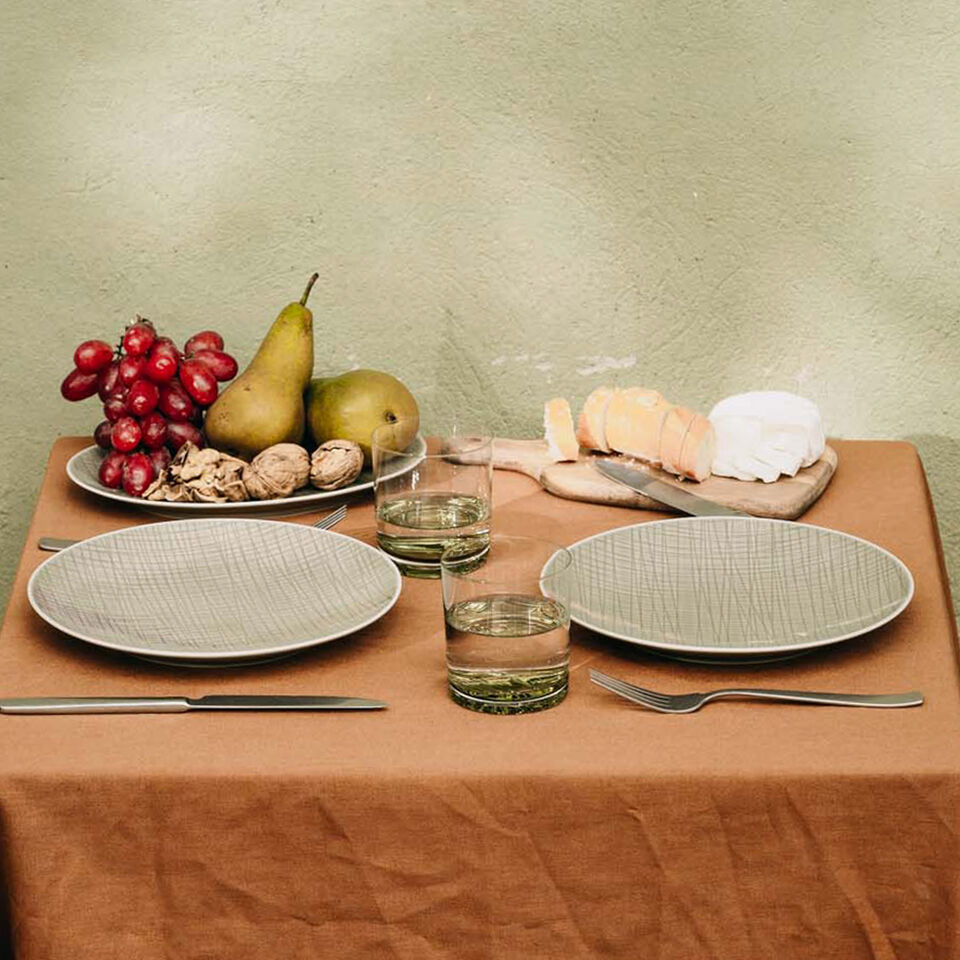 Zeit zu zweit mit Mesh Seitliche Ansicht eines für zwei Personen gedeckten Tisches mit orangefarbiger Decke, Mesh Tellern, Mesh Gläsern, Weintrauben, Birnen, Walnüssen, Baguette und Weichkäse.