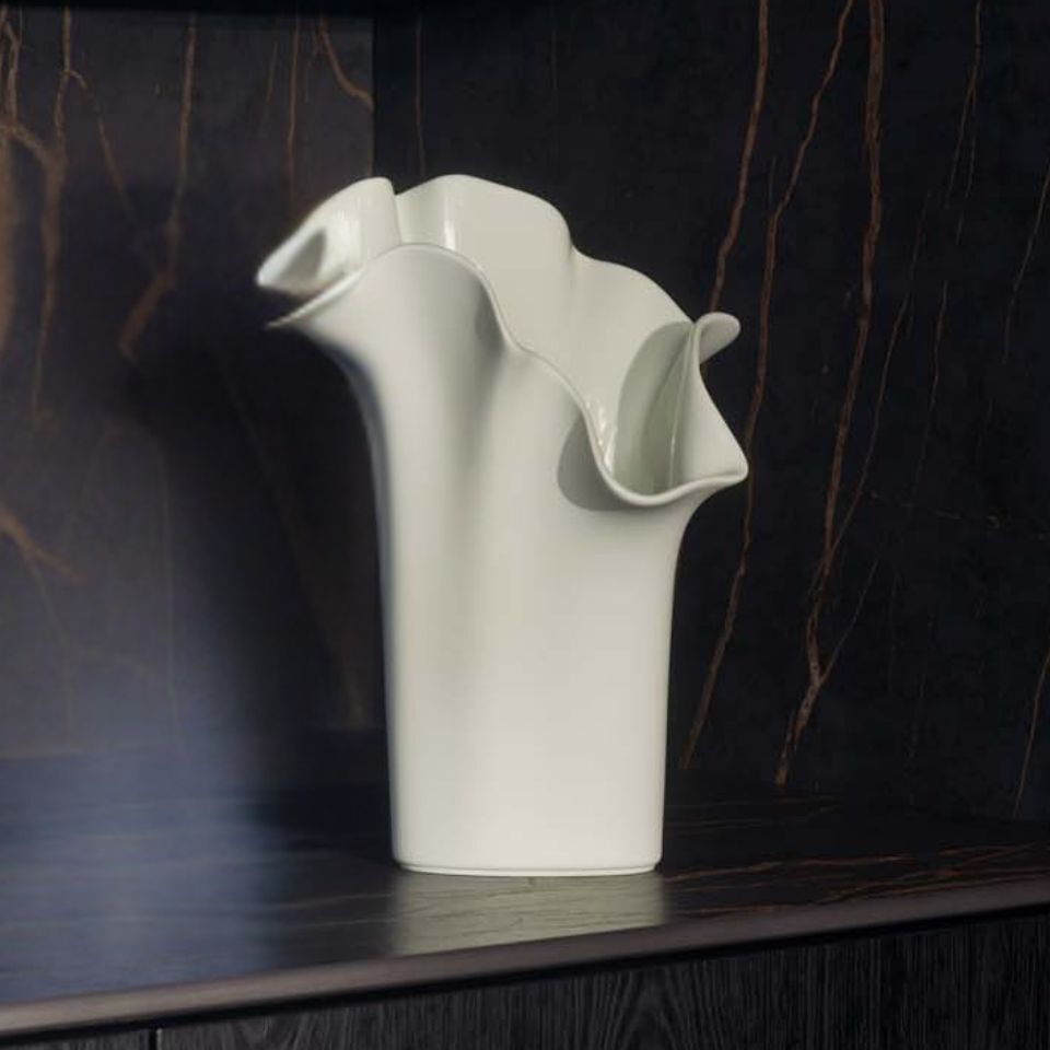 A fan-shaped white vase with vertical ridges, placed on a stone mantel with cascading dried flowers.