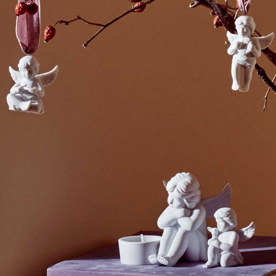 White porcelain angel figurines, one with a candle holder, two hanging from a red-berried branch.