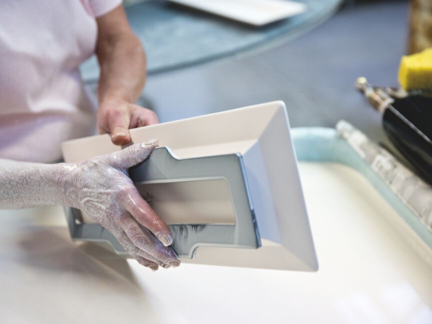 Porzellanherstellung: Ein Mitarbeiter entnimmt vorsichtig ein frisch gegossenes rechteckiges Porzellanst&uuml;ck aus einer Form.