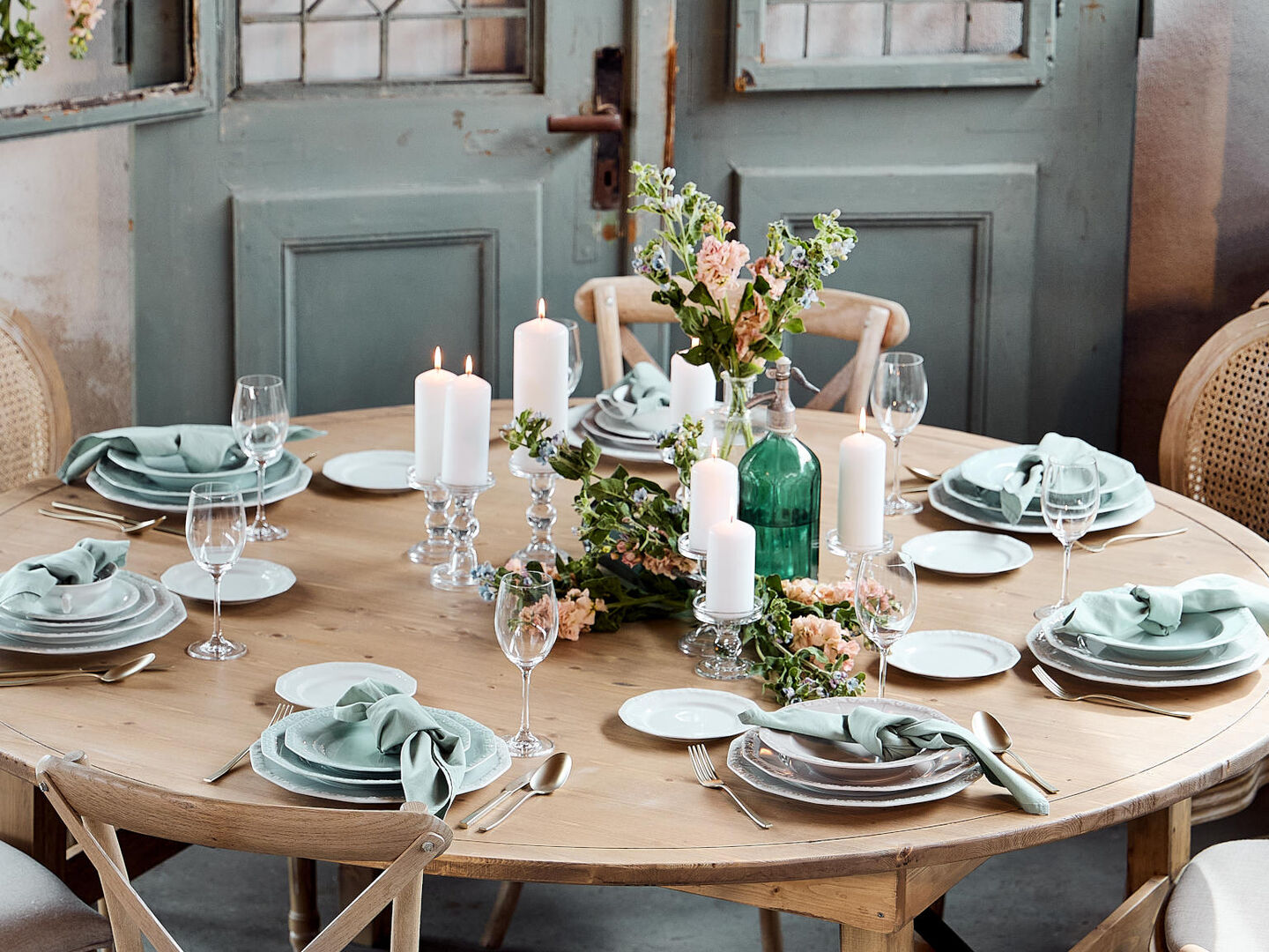 View from above of plates of different sizes by Maria Weiss, Maria Pale Orchid ung Maria Pale Mint, decorated with golden cutlery, candles and dried flowers lying on a linen tablecloth.