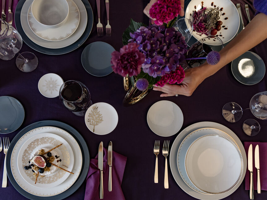Festlich gedeckter Weihnachtstisch in Violetttönen mit elegantem Porzellan, goldenen Details und Blumendekoration aus Hortensien und Chrysanthemen.