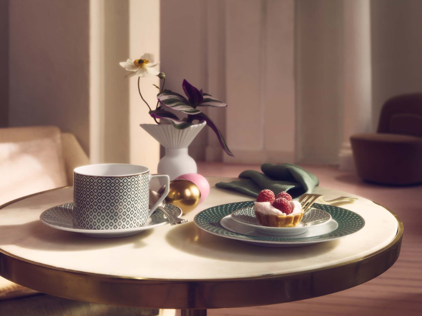 Tasse &agrave; caf&eacute; Rosenthal de forme cylindrique moderne, avec bord droit et motif discret, assortie &agrave; une soucoupe, dispos&eacute;e sur une table ronde.