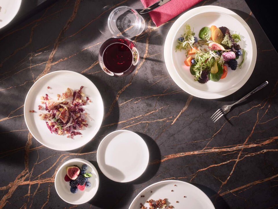 Gedeckter Tisch mit verschiedenen Tellern mit verschiedenem Essen gef&uuml;llt sowie Besteck und Weingl&auml;ser