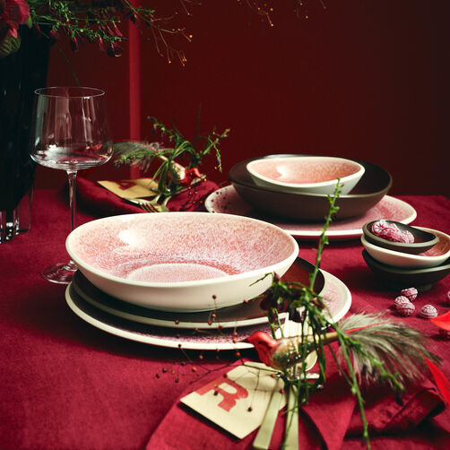 Verschiedene Junto Rose Quartz und Bronze Teller aufeinander gestapelt auf festlich gedecktem Weihnachtstisch mit S&uuml;&szlig;igkeiten und Dekozweigen