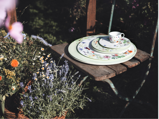 Romantisch gedeckter Gartentisch mit floralen Bone China Porzellan von Rosenthal: Feine Teller und Tasse mit floralem Dekor inmitten bl&uuml;hender Sommerpflanzen.