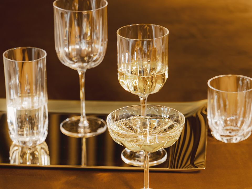 A small round table with a cup of tea, a dark green plate with a pastry topped with raspberries, a golden fork and spoon, and a white flower placed nearby.